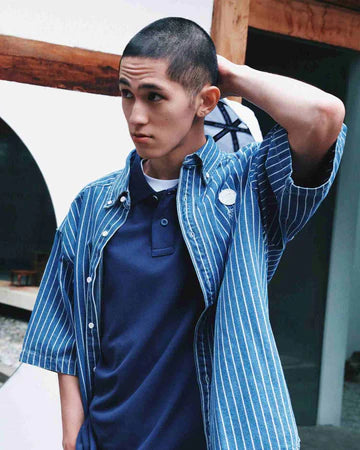 Person wearing a blue striped shirt layered over a dark t-shirt, standing outdoors