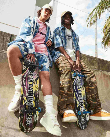 Two people sitting on a blue wall with skateboards, wearing stylish clothing.