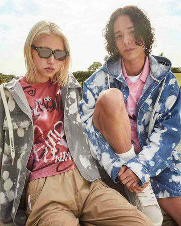 Two people wearing patterned jackets and casual outfits, sitting outdoors in a relaxed pose
